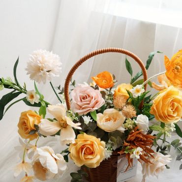 A beautiful basket filled with yellow, peach, and white flowers.