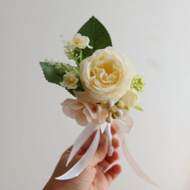 Hand holding a delicate white and cream floral boutonniere with ribbons.
