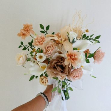A hand holding a delicate bouquet of pastel-colored flowers against a plain background.