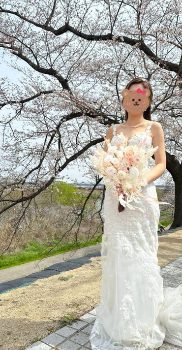 Bride in a white lace dress holding a floral bouquet under cherry blossoms.
