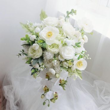 Elegant bouquet of white flowers with green accents on a soft white fabric.