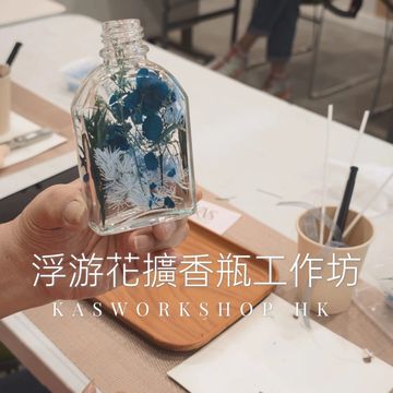 A hand holding a glass bottle filled with blue and white flowers at a workshop.