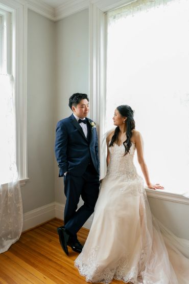 Bride and groom posing by a large window in a bright room.