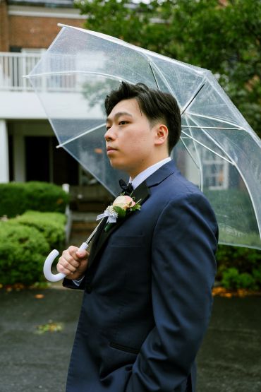 Man in suit holding a clear umbrella outdoors.