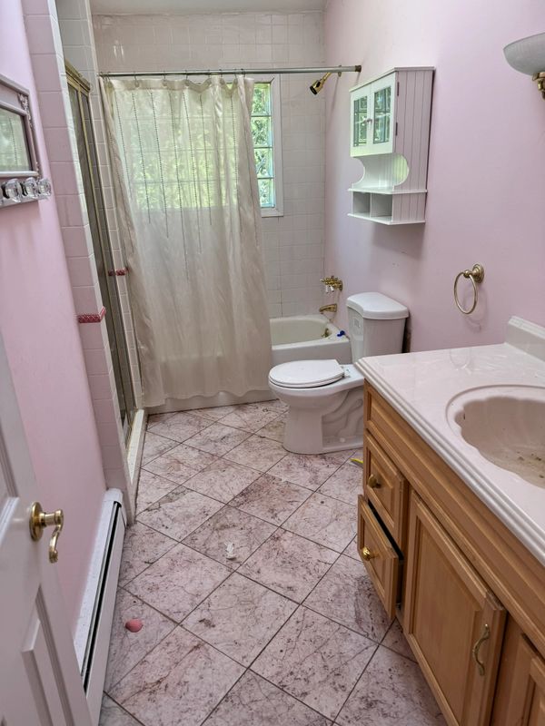 Small bathroom with pink walls, tiled floor, and wooden vanity.