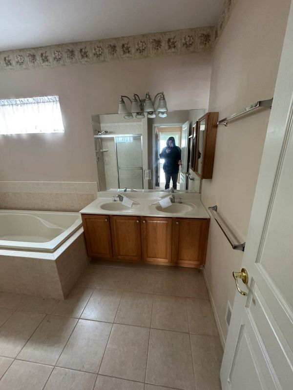 Bathroom with double sinks, wooden cabinets, bathtub, and a mirror reflecting a person taking a photo.