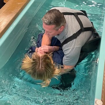 A man baptizing a woman in a pool.