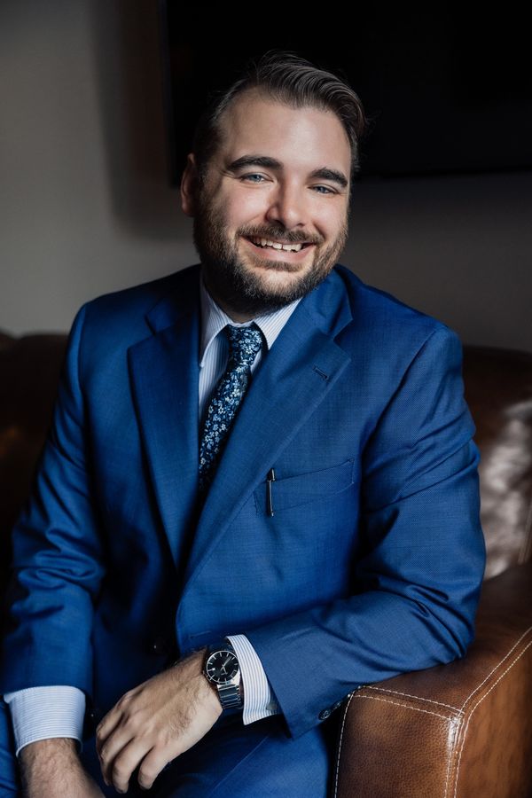 a white, male wearing a blue suit and blue tie smiling