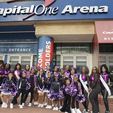 A group of cheerleaders and women in purple and black outfits posing outside Capital One Arena.