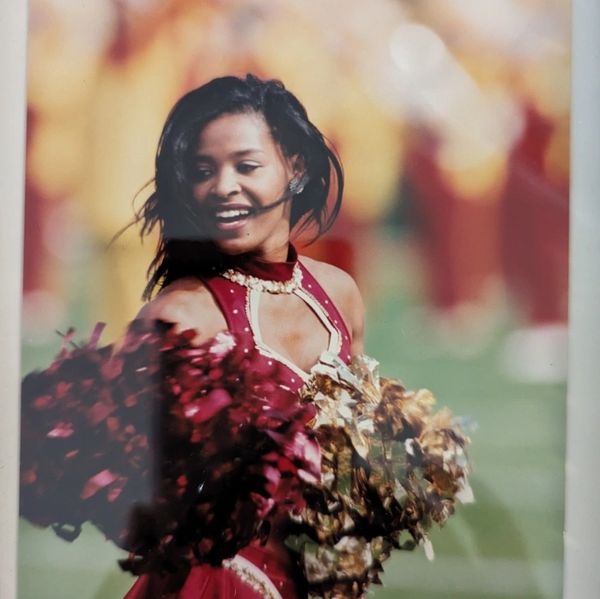 Cheerleader in red uniform performing with pom-poms at a sports event.