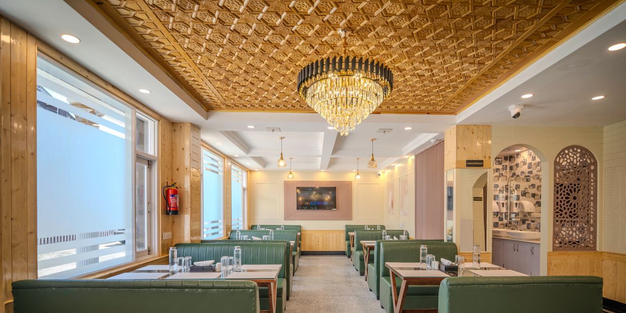 Elegant restaurant interior with green seating and a decorative wooden ceiling.
