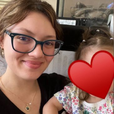 Woman smiling with child whose face is covered by a heart emoji.