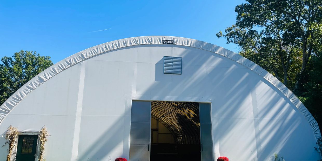 A large white fabric-covered barn under a clear blue sky with trees around.