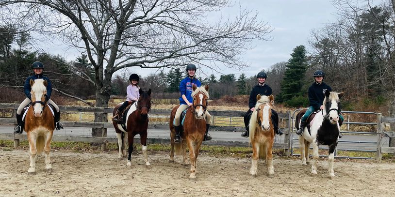 Five people riding horses in a row outdoors on a cloudy day.