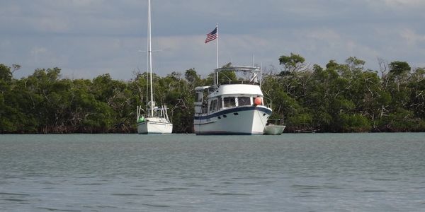Two boats anchored near a lush mangrove shoreline under a cloudy sky.