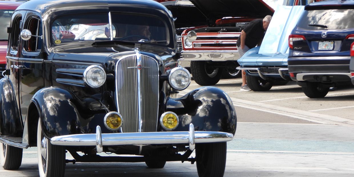A shiny black vintage car at a classic car show with other vehicles in the background.