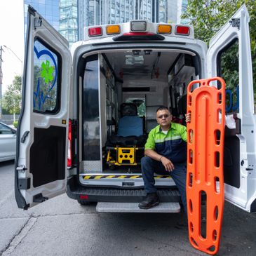 Paramedic sitting at the back of an open ambulance holding an orange stretcher board.