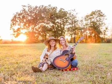 Two women music duo sitting in a field. They are a harmony musical duo known by the name, The Sparr