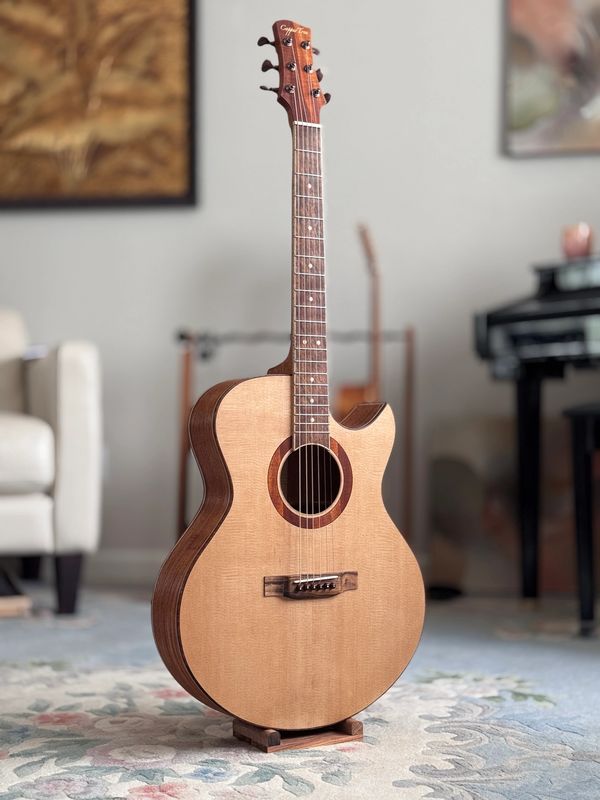 Acoustic guitar standing on a rug in a living room.