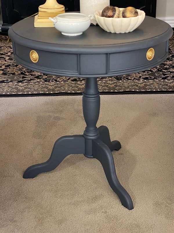 Elegant round black side table with gold knobs and decorative items.