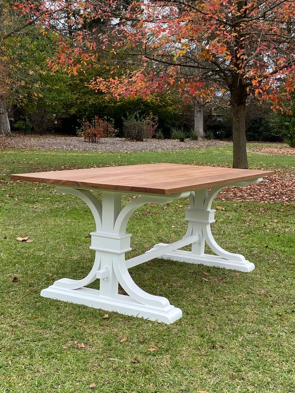 Wooden table with white trestle legs on green grass under autumn trees.