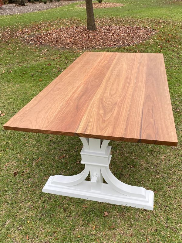 Wooden table with white base set outdoors on grass.