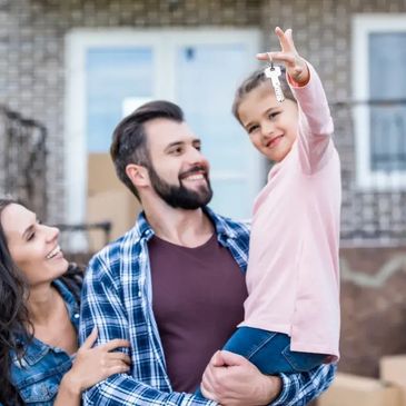 A happy family smiling and holding up keys in front of their new home after a successful move
