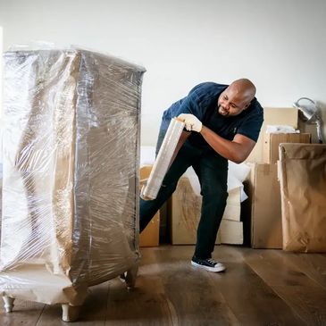 professional mover securely wrapping a large piece of furniture with protective plastic stretch wrap