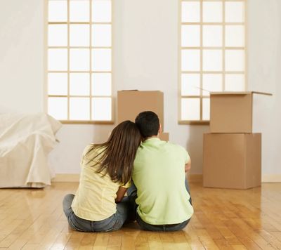 A couple sitting on the floor of their new home, resting among moving boxes in a bright, empty room.