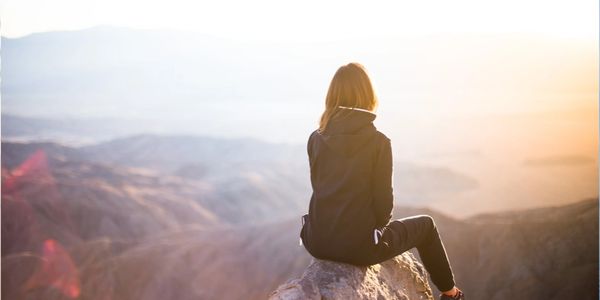 A person sitting on a rock overlooking a mountainous landscape at sunrise.
