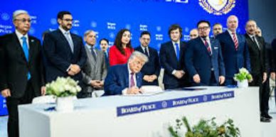 A man signs a document at a formal event with a group of officials standing behind him.