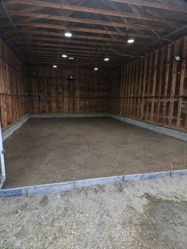 Empty wooden garage with dirt floor and lights.