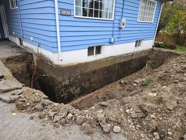 Excavation around a blue house foundation for construction or repair.