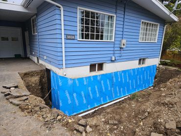 Blue house foundation waterproofing with exposed soil around.