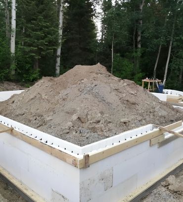 Concrete foundation with a ladder and dirt piles in a forested area.