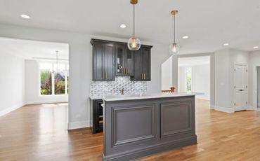 Modern kitchen island with dark cabinets and pendant lights in a bright open space.