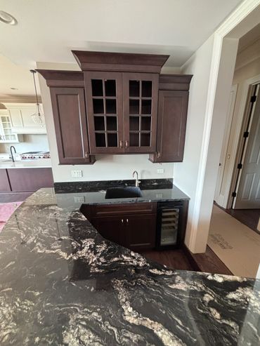 Luxurious kitchen bar with dark granite countertop and dark wood cabinets.