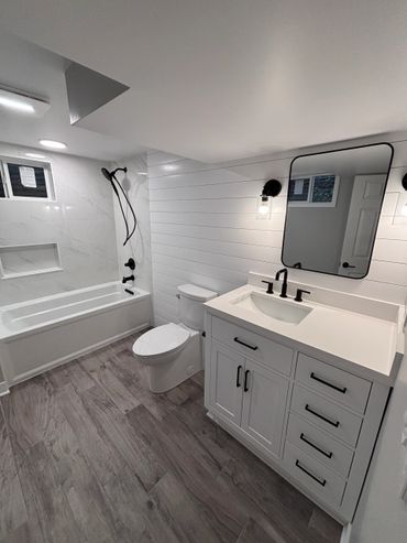 Modern white bathroom with black fixtures and wood-style flooring.