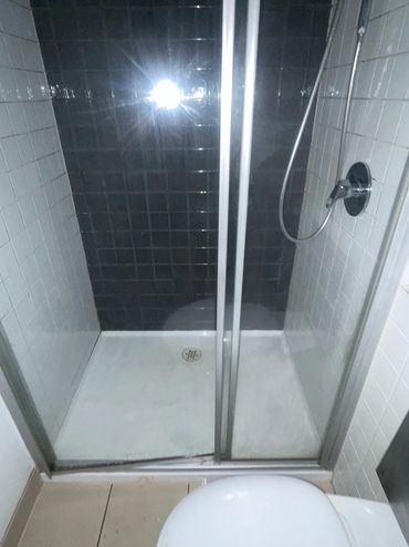 A tiled shower stall with sliding glass doors and a handheld showerhead.
