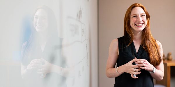 A woman smiling in front of a whiteboard planning out a design process