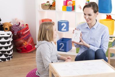 Child counselor showing drawings to little smart girl with ADHD
