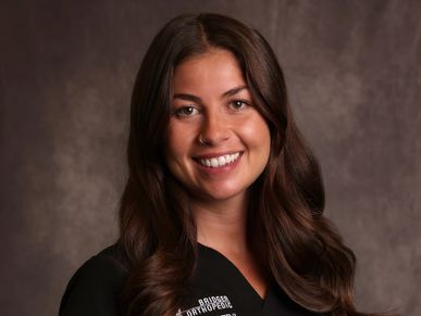Smiling healthcare professional in black scrubs posing against a neutral backdrop.