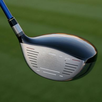 Close-up of a golf driver club head with a blue shaft against a green background.