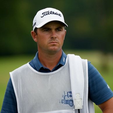 Serious golfer in a Titleist cap and caddie vest on a golf course.
