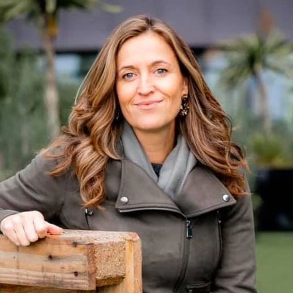 Smiling woman with wavy hair outdoors in a casual coat.