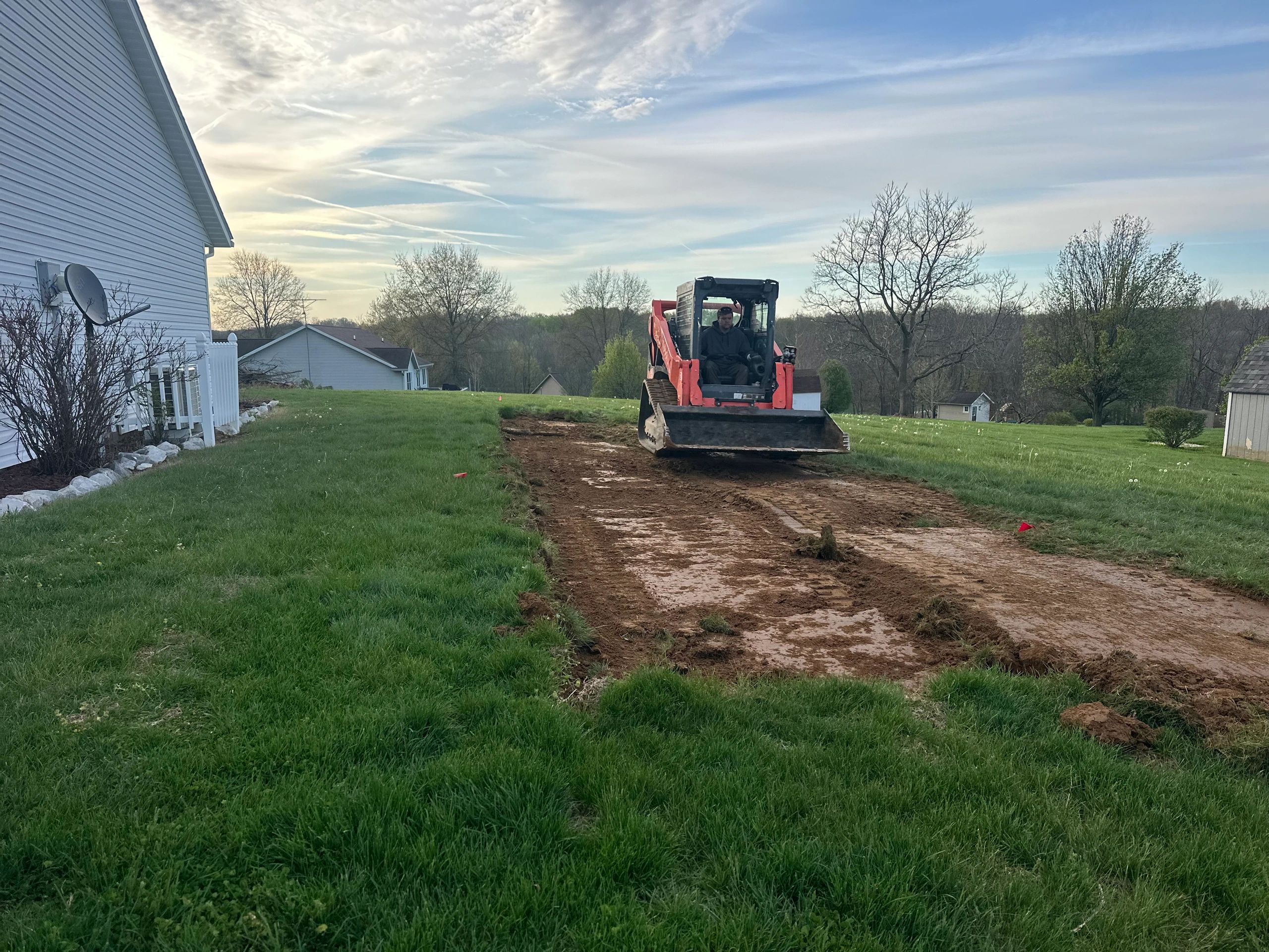 A man operating a bulldozer clearing a dirt path in a grassy yard.