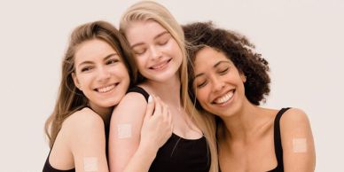 Three smiling women with vaccine bandages on their arms.