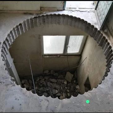 A large circular hole with scalloped edges in a concrete floor revealing a room below.
