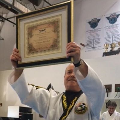 Man in martial arts uniform proudly holds up a framed certificate.