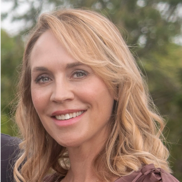 Smiling woman with blonde hair in a mauve dress outdoors.